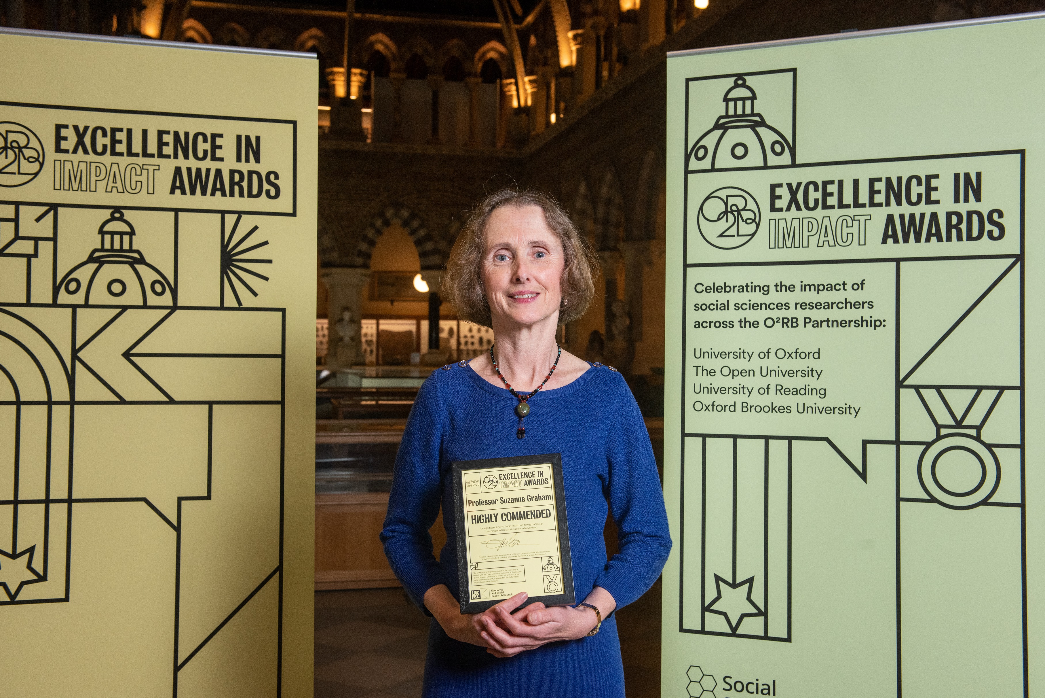 Professor Suzanne Graham holds the Highly Commended impact award, flanked by event branding at the awards reception