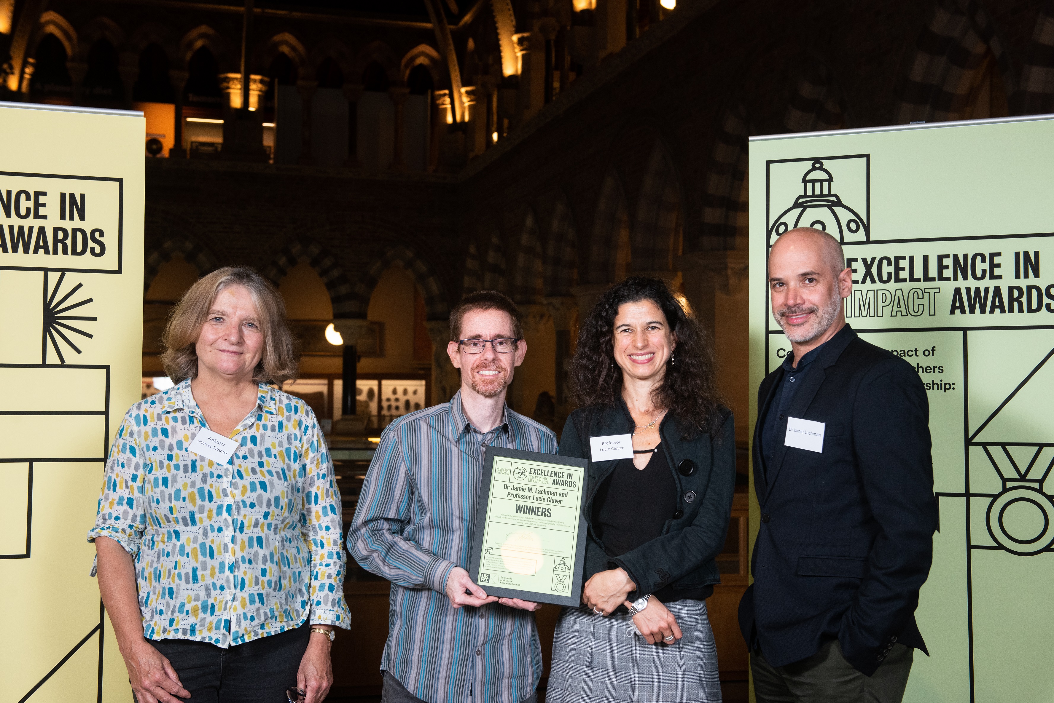 Jamie Lachman, Lucie Cluver, and colleagues smile as they hold their Impact Awards winners certificate, in front of the O2RB Excellence in Impact Awards event branding