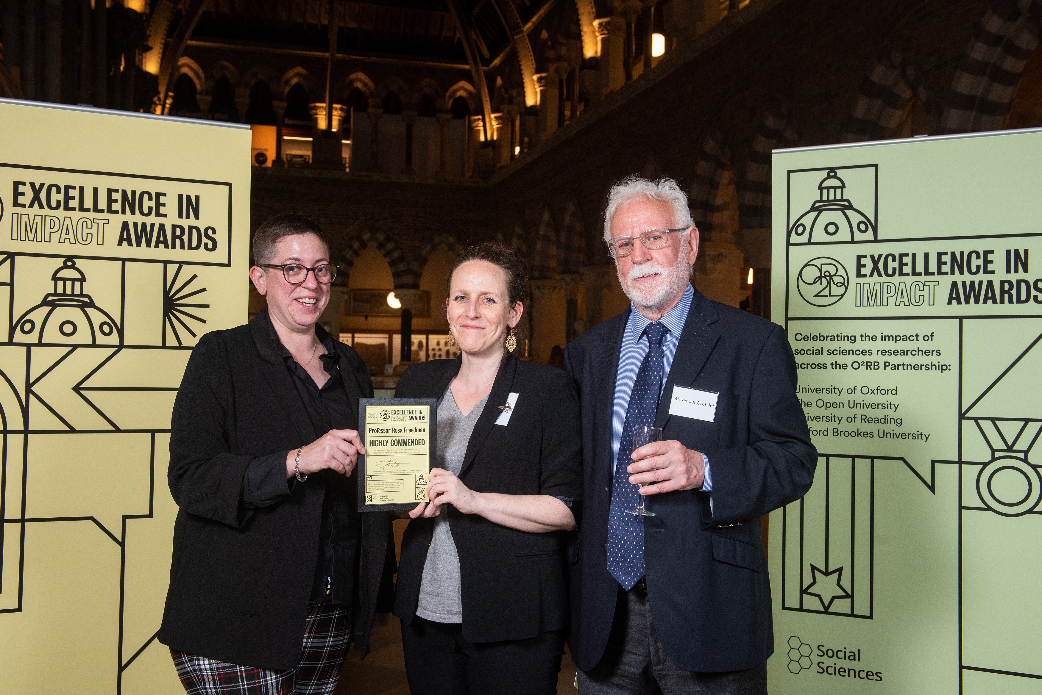 Prof Rosa Freedman holds the Highly Commended award with Sarah Blakemore and Alex Dressler, flanked by event branding at the awards reception