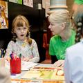 Young girl looking surprised and drawing sat at a table with a resercher