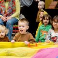 Children sat on the floor, singing and holding on to a brightly coloured play parachute