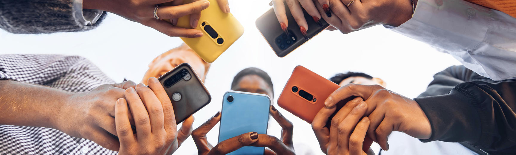 View from below of five people of diverse ethnicities standing in a huddle and using their smartphones