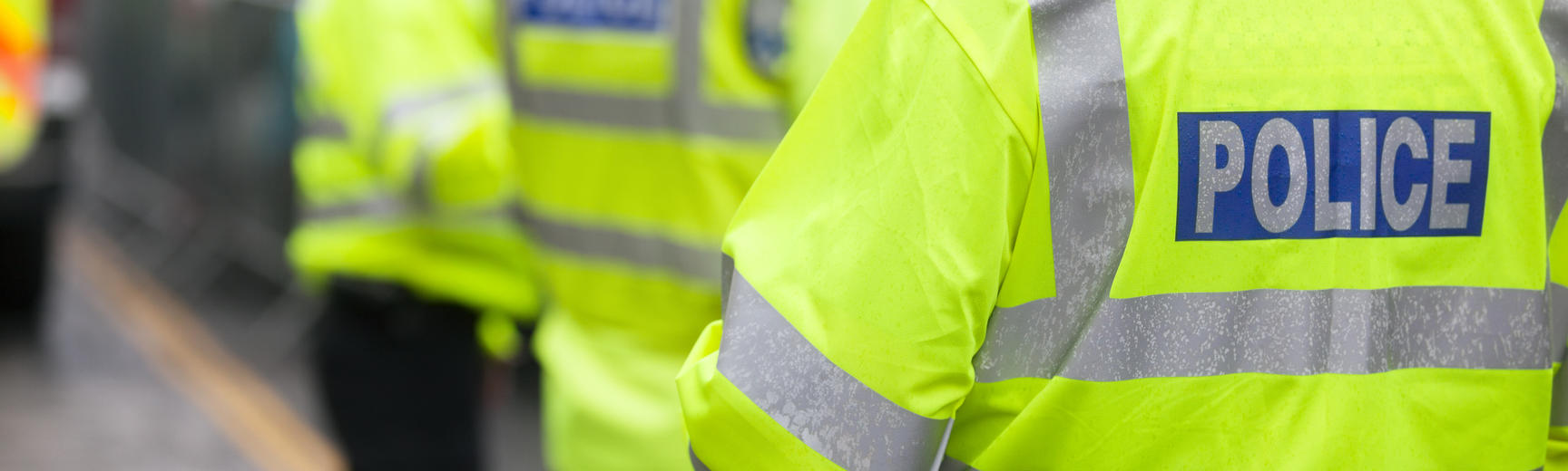 Three police officers in high-vis police jackets patrol a street