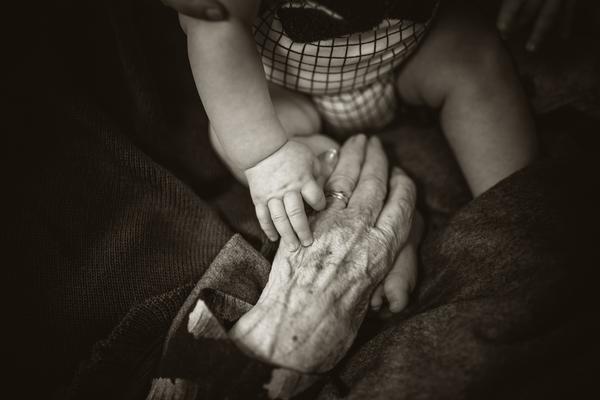 A baby holds an old lady's hand