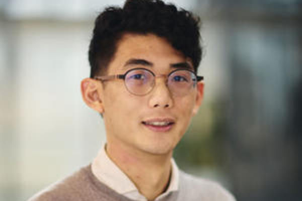 Dr En Hua Hua with short dark hair wearing glasses, a light shirt, and a beige sweater, posing indoors.