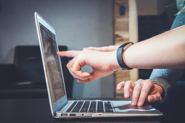 A person points to something on a computer screen to guide the computer user, whose fingers are moving the mouse