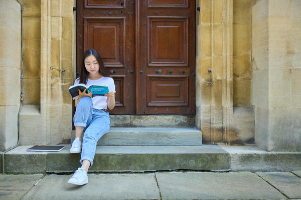 An Oxford University student sat on the steps of a building reading a text book