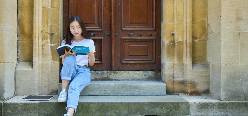An Oxford University student sat on the steps of a building reading a text book