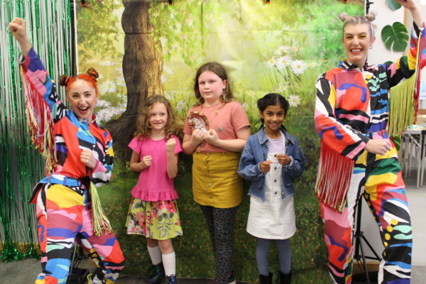 Superpillars assemble! Two adults, dressed as mutli-coloured, cheering butterflies, and three smiling children, pose as “superpillars” in front of a forest backdrop.