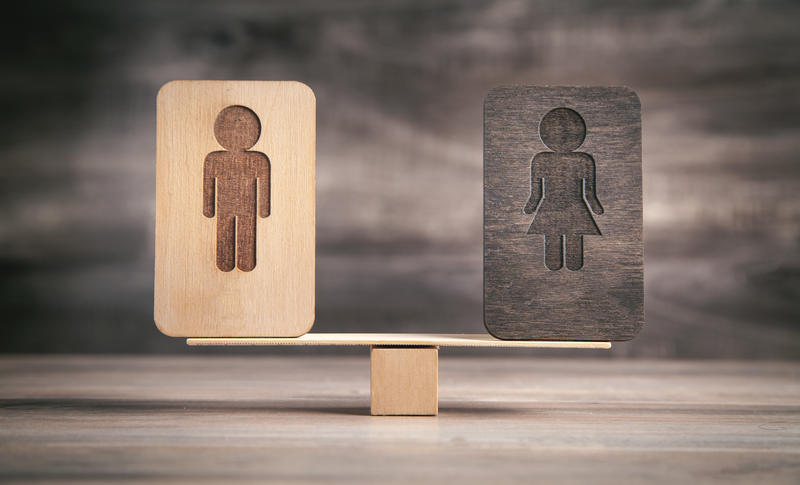 Wooden blocks with male and female symbols balanced on a seesaw, representing gender equality.