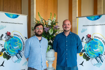 Alessio Bertolini and Jonas Valente smile to camera. In the background is the Impact Awards branding and a flower arrangement.