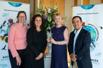 Four Young Lives team members smile and hold the Developing Impact trophy. In the background is the Impact Awards branding and a flower arrangement.
