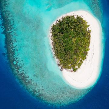 Birdseye view of a small tropical island with very little vegetation and land mass, surrounded by white sand and huge, dark blue ocean
