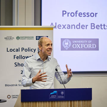 Prof Alexander Betts animatedly addresses an audience from a lectern