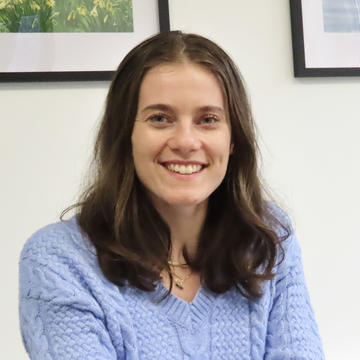 Faith Inch has shoulder length brown hair, wearing glasses smiling at the camera.