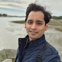 Dr Avidesh Seenath Dr Seenath has short black hair. He is standing outside by a river, wearing a navy quilted jacket.