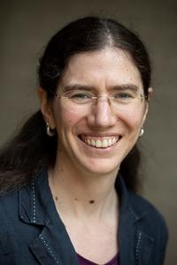 Dr Elizabeth Baldwin Dr Baldwin has long dark hair, tied in a low ponytail. She is wearing glasses with no frame and smiling widely.