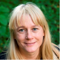 Dr Nicole Dingwall Dr Dingwall has long blonde hair with a fringe and blue eyes. She is standing in front of some green foliage and smiling.
