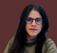 Dr Uttara Shahani Dr Shahani has long dark hair and large dark-rimmed glasses. She is wearing a grey jumper.