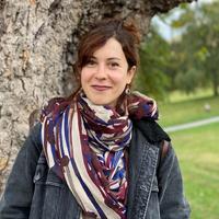 Dr Ana Valdivia Dr Valdivia has long brown hair which she is wearing tied up. She is standing by a tree wearing a patterned cream, purple and blue scarf.