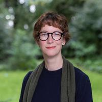 Dr Catherine Hamilton Dr Hamilton has short auburn hair and is wearing dark-framed round glasses. She is wearing a navy jumper and dark green scarf, standing in a garden.