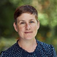 Prof Kathryn Eccles has a short pixey hair cut, wearing a dark blue top, smiling at the camera. 