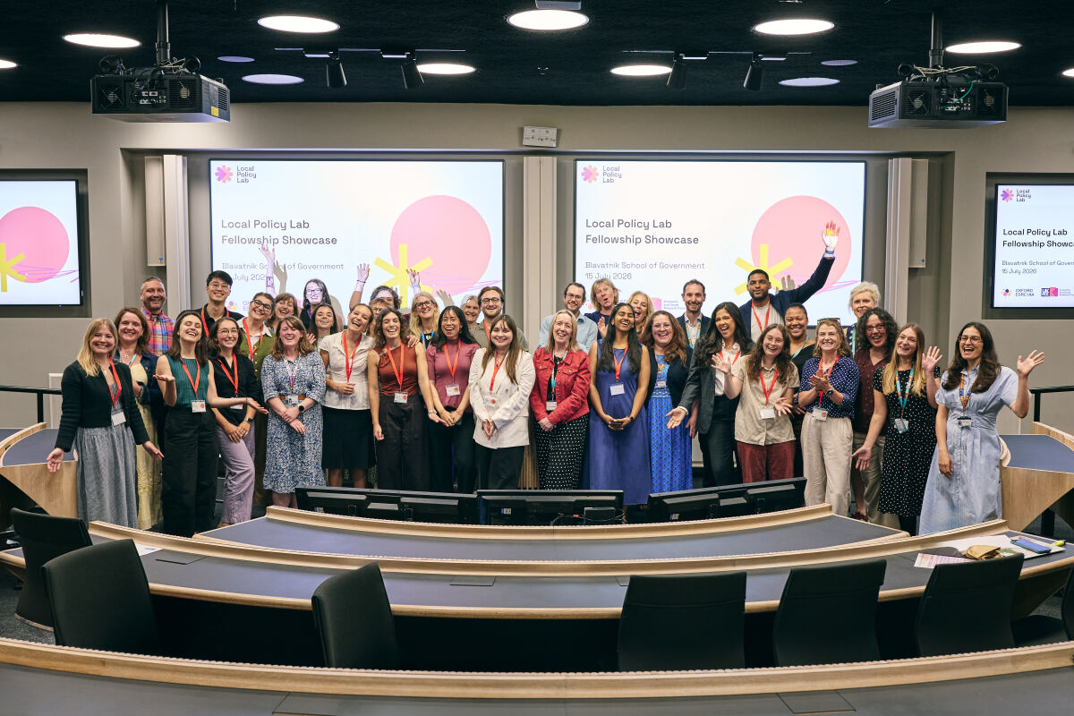 A group of over 20 students and facilitators stand in front of the screens at the end of the Local Policy Lab Fellowship showcase event