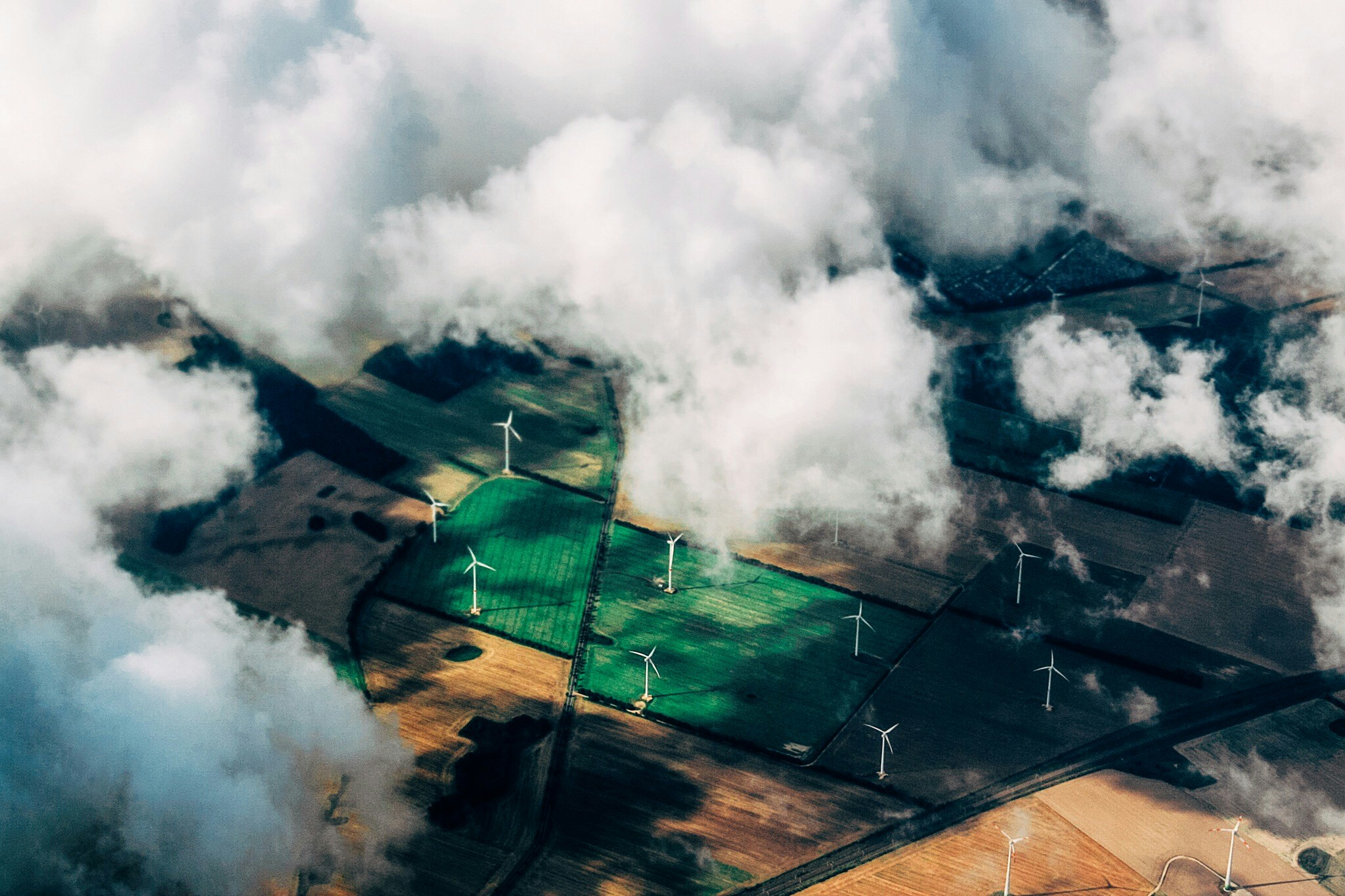Aerial view of wind turbines in green and yellow field half hidden by white clouds