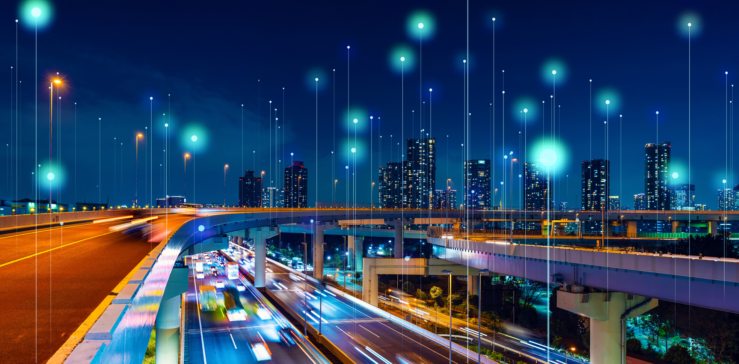 Blurred night-time shot of a city scape, showing a busy highway and flyover with lots of fast-moving traffic