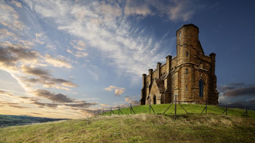 A historic chapel sits atop a hill with sunset in the background