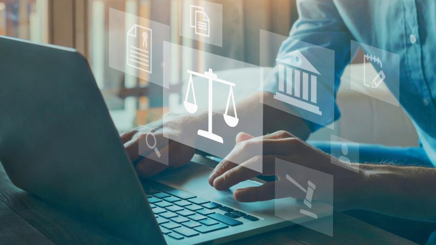 Lawyer types on a laptop surrounded by graphics images of scales of justice, gavel, and data graphics