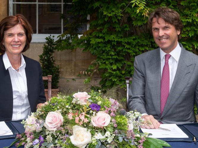 Professor Louise Richardson, Vice-Chancellor of Oxford and Hubert Keller, Co-Senior Partner of the banking group Lombard Odier, sit at a table decorated with flowers as they sign a multi-year partnership to foster sustainable finance & investment research