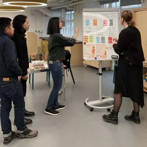 Three young people point at a poster while a researcher listens