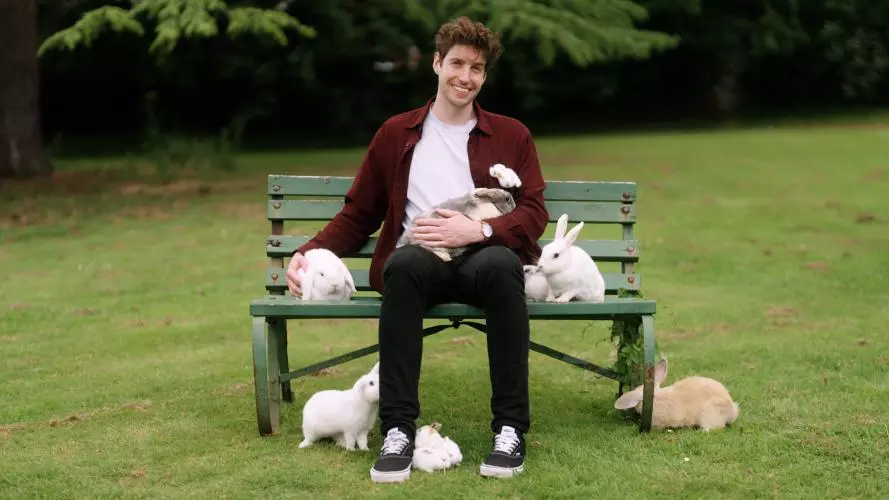 Man sitting on a garden bench with six or seven rabbits around him