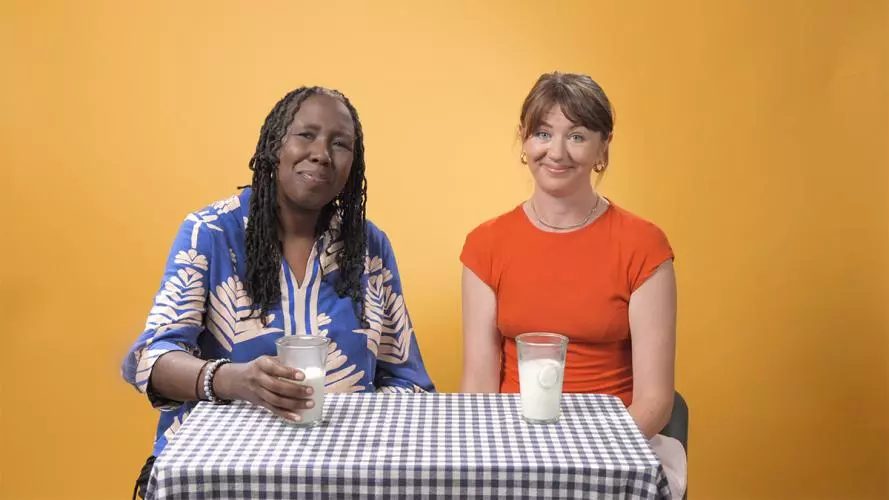 Two women sit at a table, each has a glass of milk in front of them