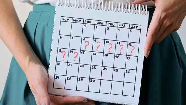 The hands of a woman holding a calendar, which shows 7 consecutive days marked with a question makr