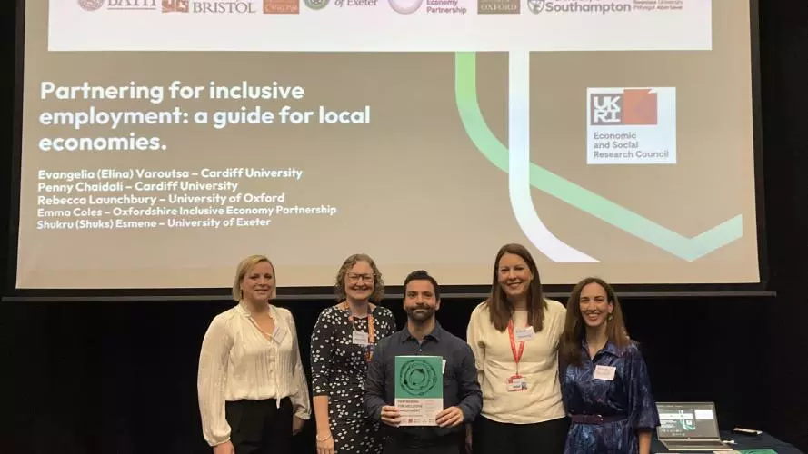 Five people stand in front of a presentation slide titled "Partnering for inclusive employment: a guide for local economies.