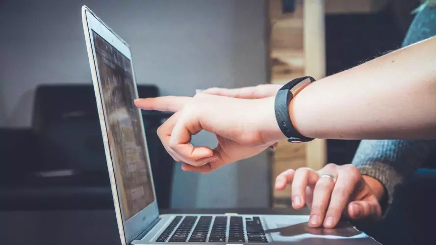 A person points to something on a computer screen to guide the computer user, whose fingers are moving the mouse