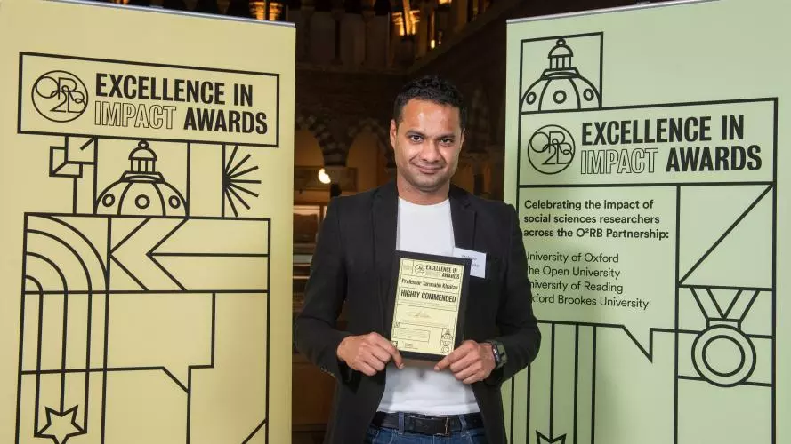Professor Tarunabh Khaitan holds his Highly Commended impact award, flanked by event branding at the awards reception
