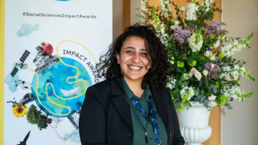 Dr Mona Ibrahim smiles to camera. In the background is the Impact Awards branding and a flower arrangement.
