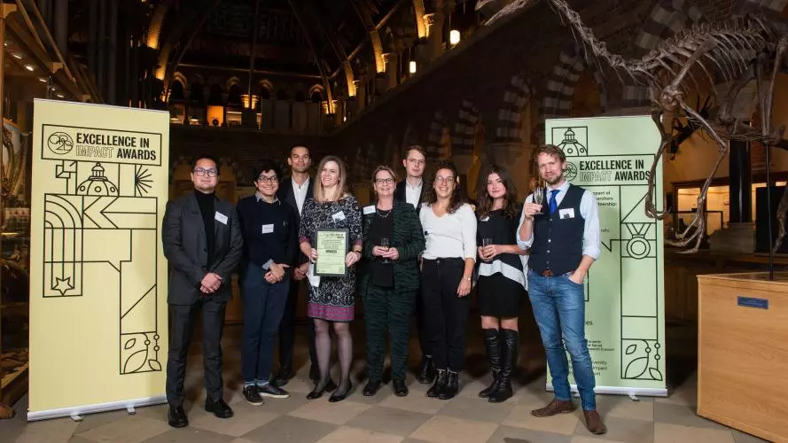Professor Melinda Mills, Dr Jennifer Beam Dowd, and colleagues from the LCDS team smile as they hold their Impact Awards winners certificate, in front of the O2RB Excellence in Impact Awards event branding