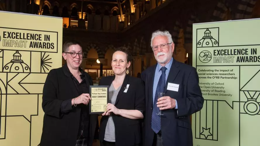 Prof Rosa Freedman holds the Highly Commended award with Sarah Blakemore and Alex Dressler, flanked by event branding at the awards reception