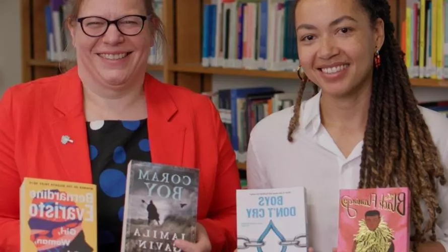 Dr Velda Elliott and Dr Zaahida Nabagereka sit side by side, smiling and holding books by authors of colour