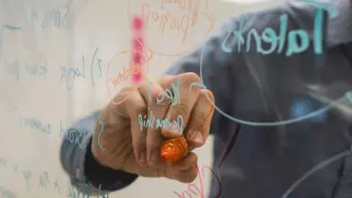 A hand writing on a glass wall with coloured felt tips
