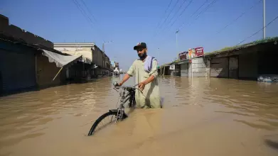 A man, thigh-deep in brown flood water, pushes his submerged bike down a street in Pakistan. Image copyright Bilawal Arbab / EPA