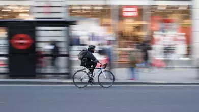 Blurred image of a cyclist cycling down a London street, past a bus stop and shops