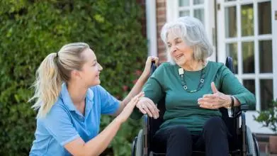 Carer pushing older woman in wheelchair outside home