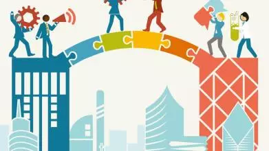 Men and women carrying objects such as a cog, a megaphone, a lightbulb, jigsaw pieces and a test tube with green liquid in, over a jigsaw bridge linking to buildings.