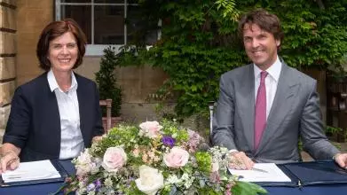Professor Louise Richardson, Vice-Chancellor of Oxford and Hubert Keller, Co-Senior Partner of the banking group Lombard Odier, sit at a table decorated with flowers as they sign a multi-year partnership to foster sustainable finance & investment research