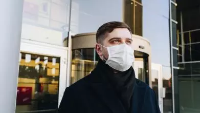 A man wearing a face mask, standing outside an office building in London